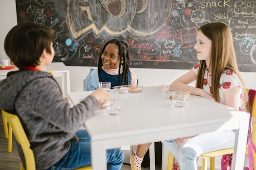 Three children engage in lively conversation during snack time at school.