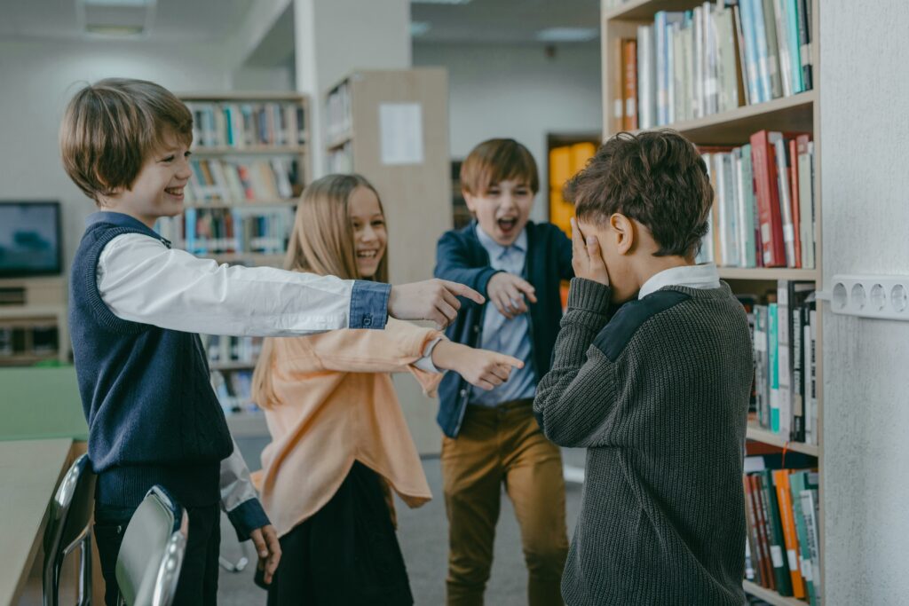 A group of children bullying another child in a school library, showcasing peer pressure and emotional distress.
